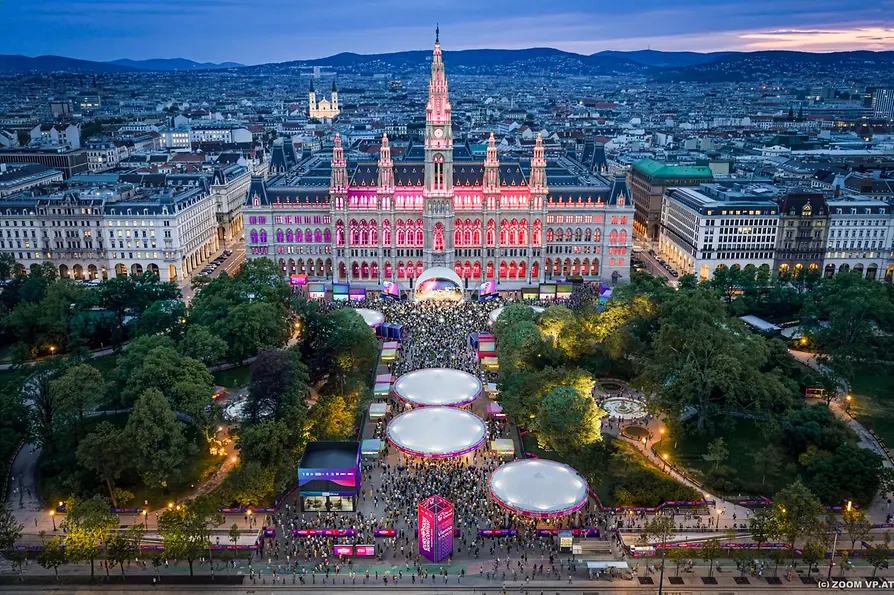 Eurovision Village at Rathausplatz Vienna 2026 at dusk with crowds, stage and illuminated city hall